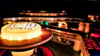 A close-up view of a brightly lit button on a pinball machine with '1000 POINTS' written on it. The button is surrounded by colorful lights and elements of the pinball machine, creating a dynamic and vibrant scene.