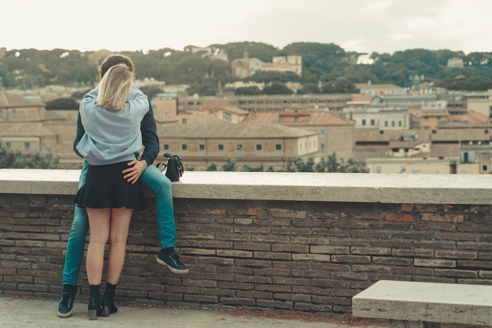 woman in gray long sleeve shirt and blue denim jeans sitting on brown concrete wall during