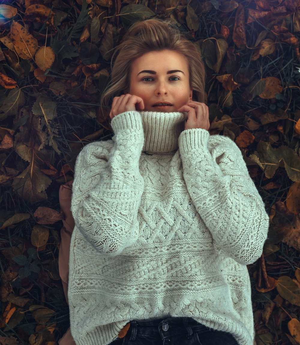 girl in white knit sweater lying on dried leaves