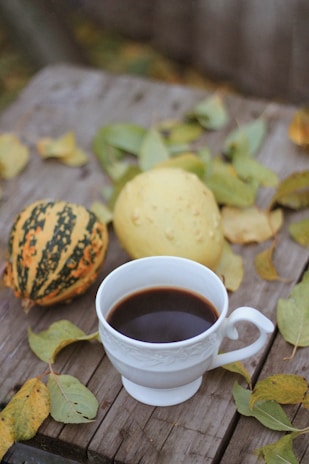 A steaming cup of coffee on a rustic wooden table surrounded by pinecones and autumn leaves.