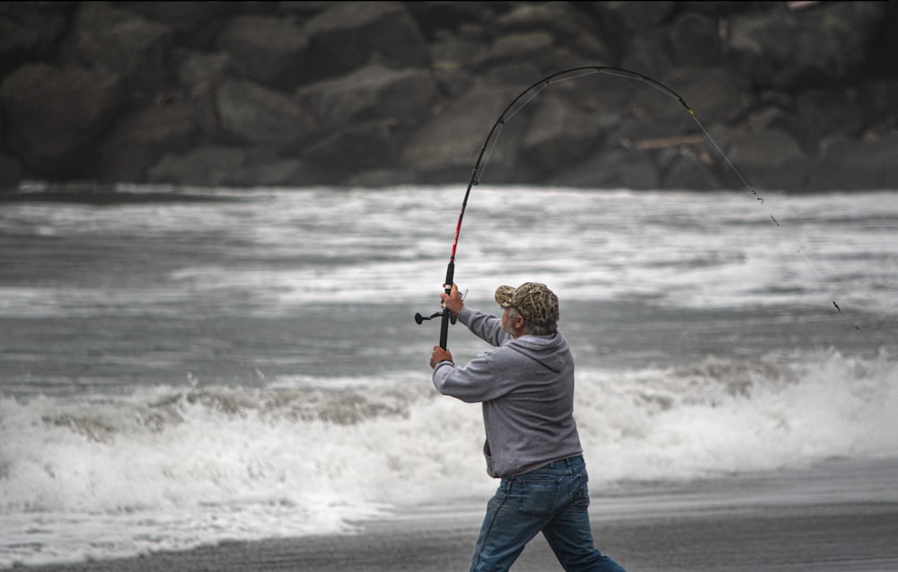 man in white shirt and blue denim jeans holding fishing rod standing on seashore during daytime