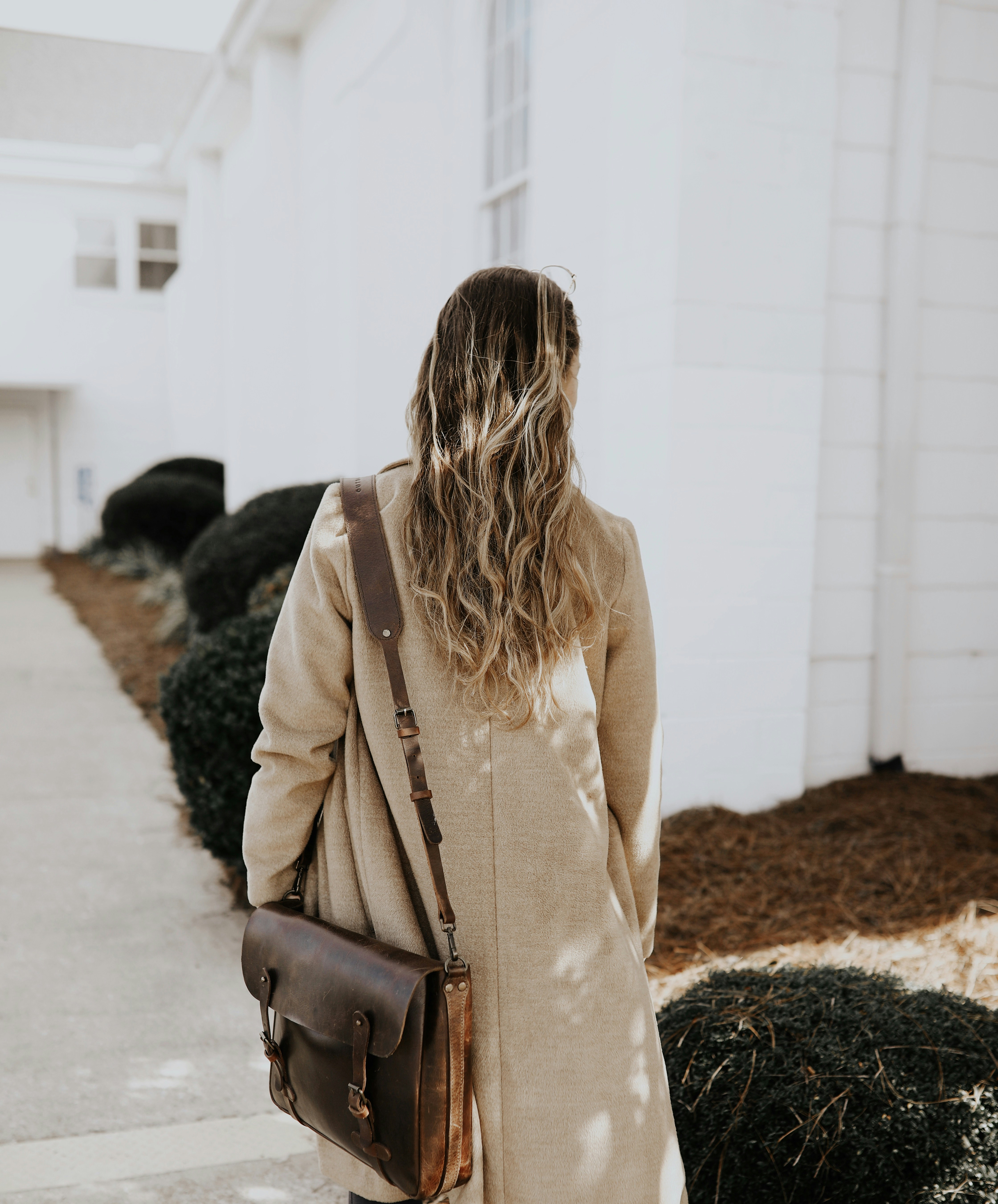 Woman wearing a neutral coat and carrying a brown crossbody bag in a bright everyday setting