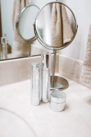 A neatly arranged bathroom featuring a ceramic tissue holder, soft cotton towels, a sleek metal spice organizer, and clear plastic storage boxes.