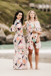 2 women in white red and blue floral dress standing on gray sand during daytime