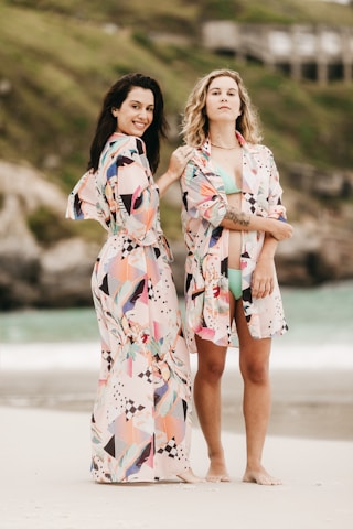 2 women in white red and blue floral dress standing on gray sand during daytime