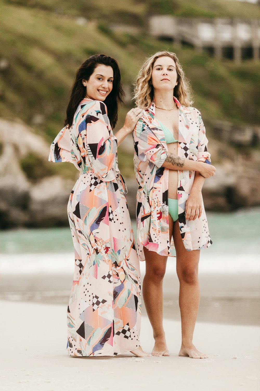 2 women in white red and blue floral dress standing on gray sand during daytime