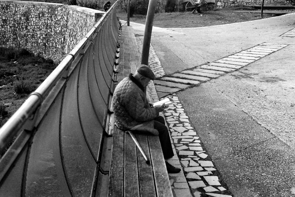 grayscale photo of man sitting on wooden bench