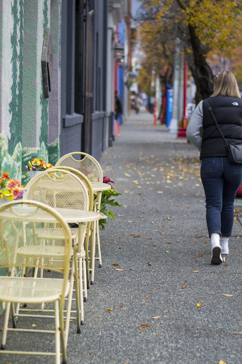 woman in black jacket and blue denim jeans walking on sidewalk during daytime