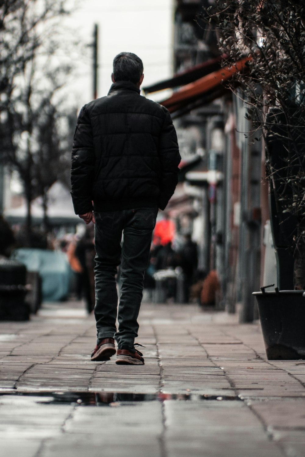 man in black jacket and blue denim jeans walking on sidewalk during daytime