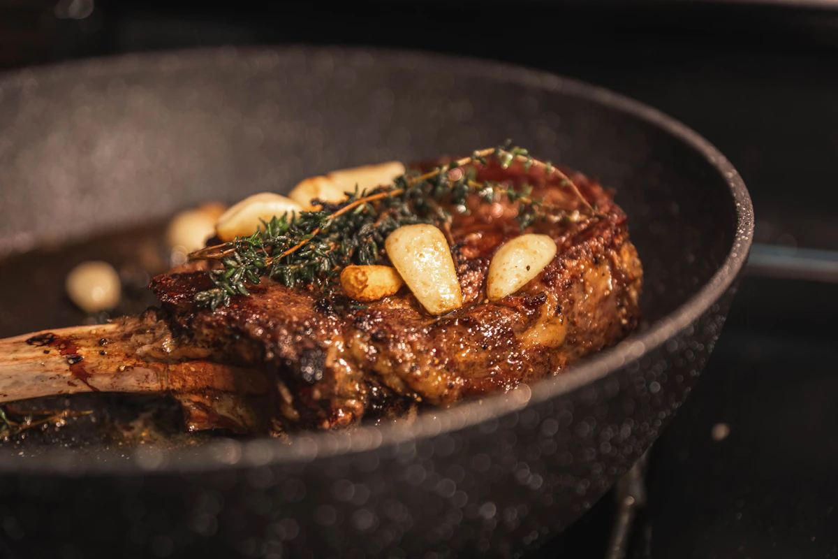 Seared tomahawk steak with garlic cloves and fresh thyme in a black pan