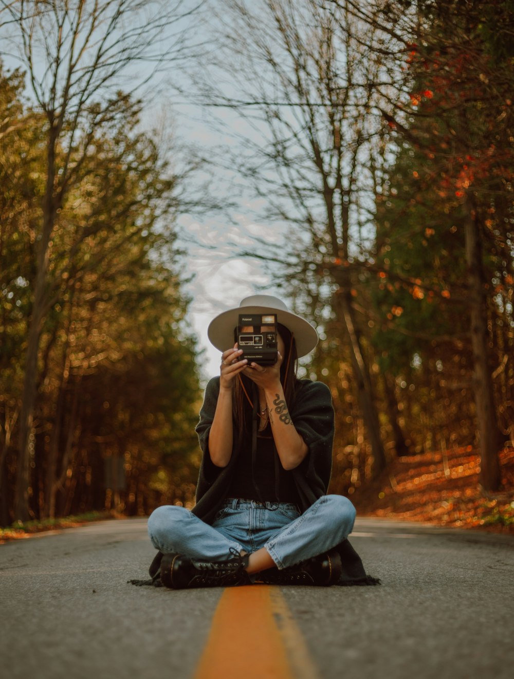 woman in gray jacket and blue denim jeans sitting on road while holding black smartphone during