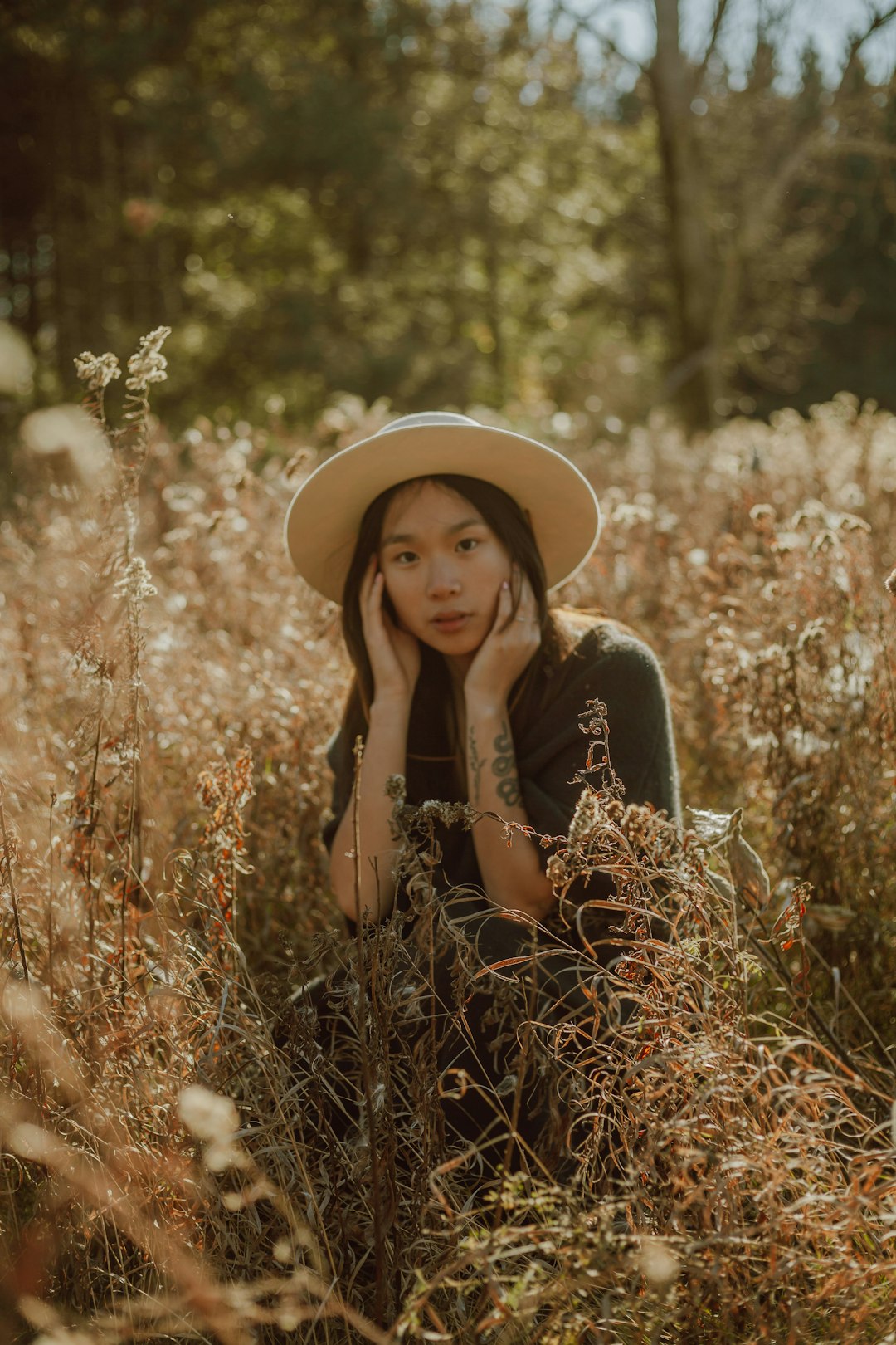 woman in brown sun hat sitting on brown grass field during daytime