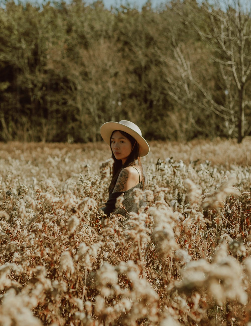 girl in black jacket and brown hat standing on white flower field during daytime