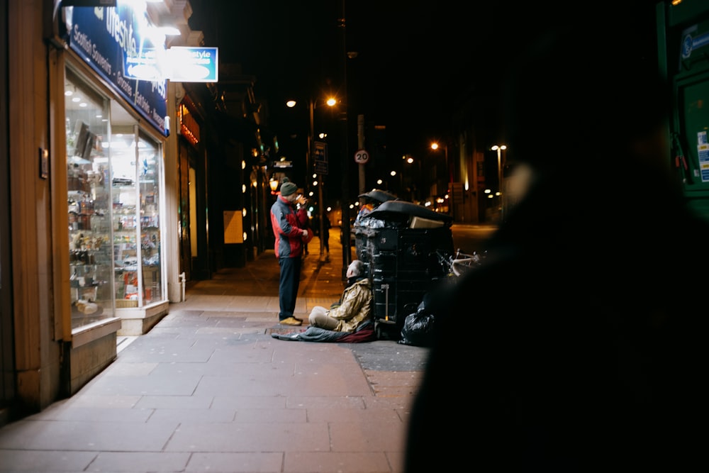 homme en veste noire et jean bleu marchant sur le trottoir pendant la nuit