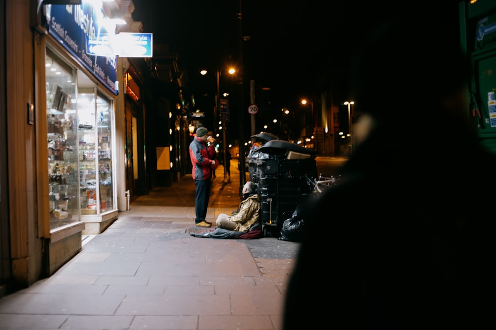 man in black jacket and blue denim jeans walking on sidewalk during night time