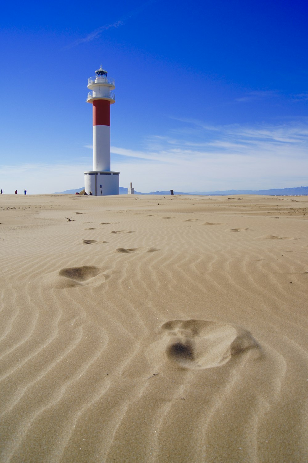 white and red lighthouse on brown sand under blue sky during daytime