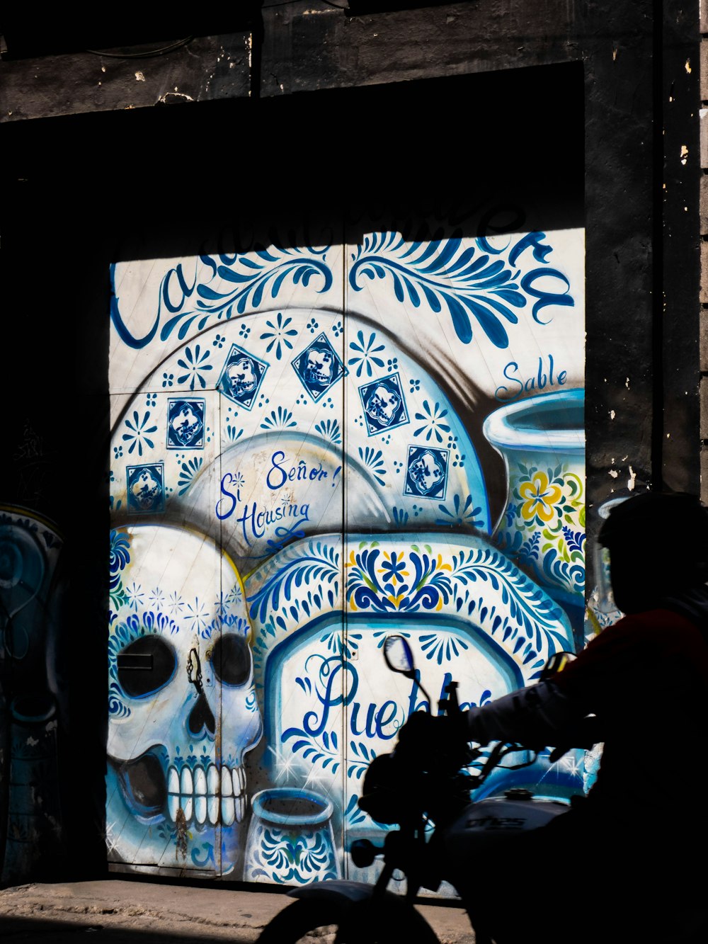 man in black jacket standing in front of blue and white floral wall