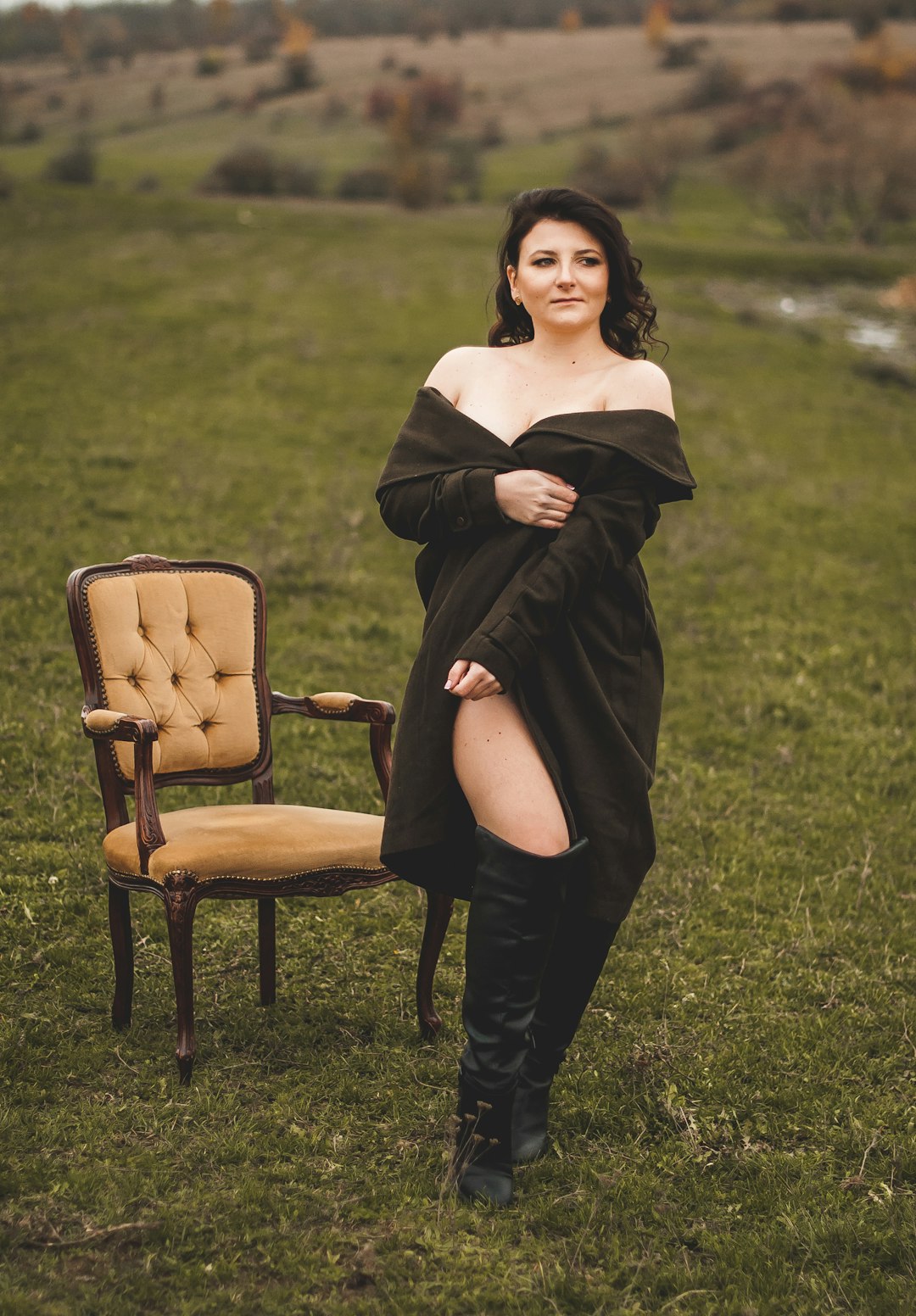 woman in black off shoulder dress and brown boots sitting on brown wooden chair