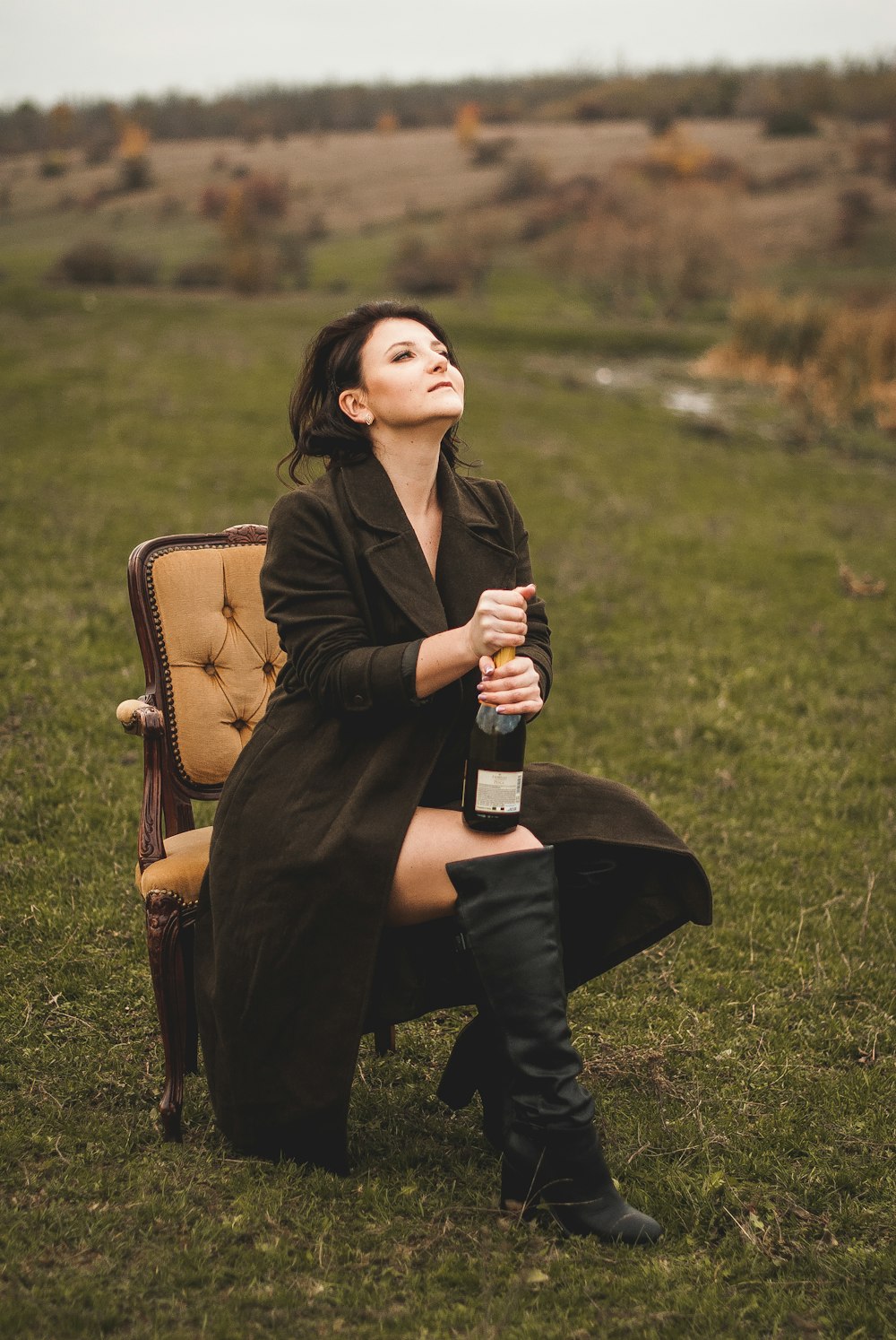 woman in brown coat sitting on brown wooden chair holding bottle