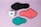 Three reusable sanitary pads in different colors are laid out on a pastel purple background. The colors include black, coral pink, and teal, each with black borders. A box with the branding 'inciclo' is placed beside the pads, featuring a design with teal shapes and floral elements.
