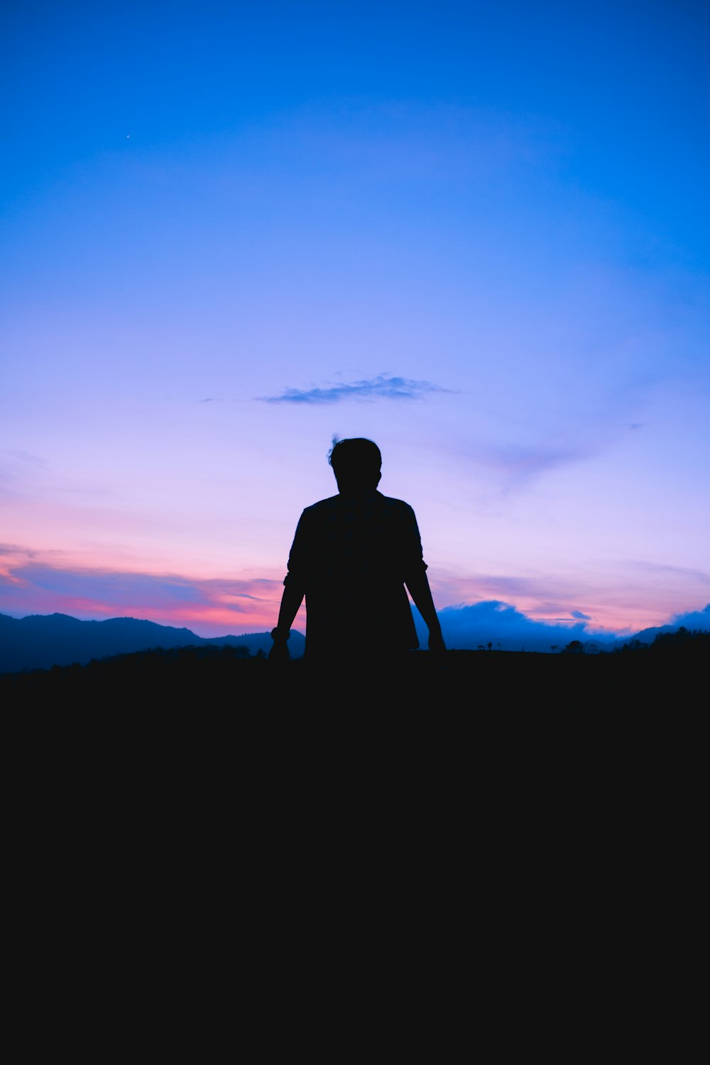 Silhouette eines Mannes, der bei Sonnenuntergang auf einem Hügel steht
