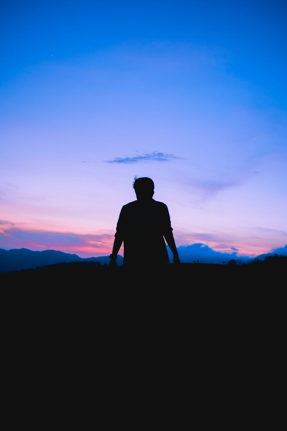 silhouette of man standing on hill during sunset