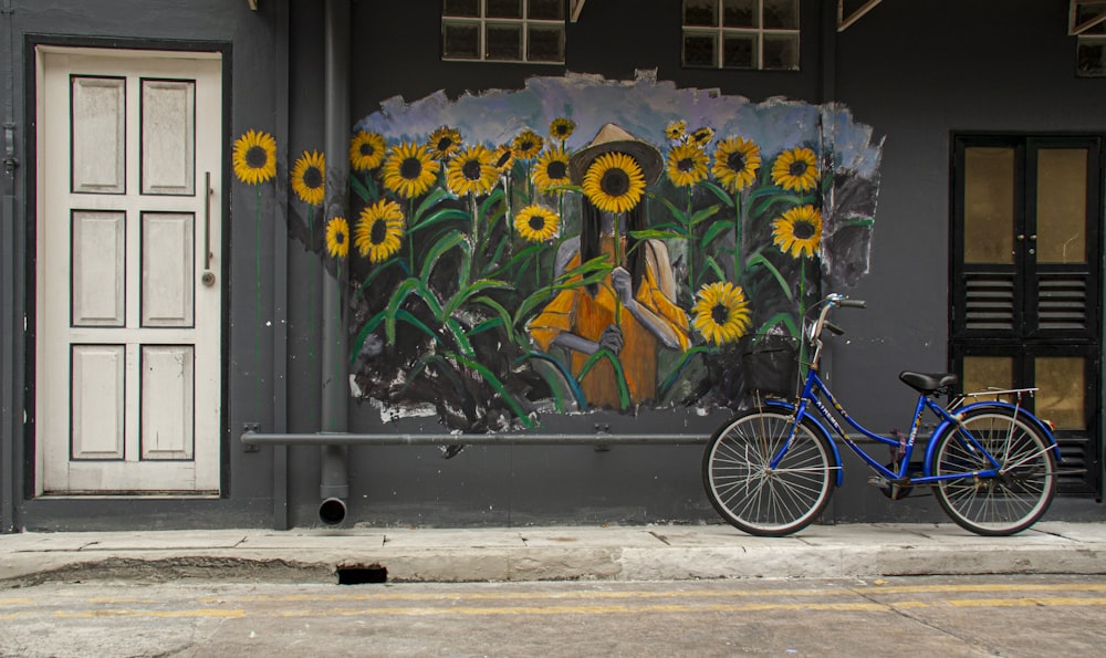 blue bicycle parked beside blue and yellow floral wall