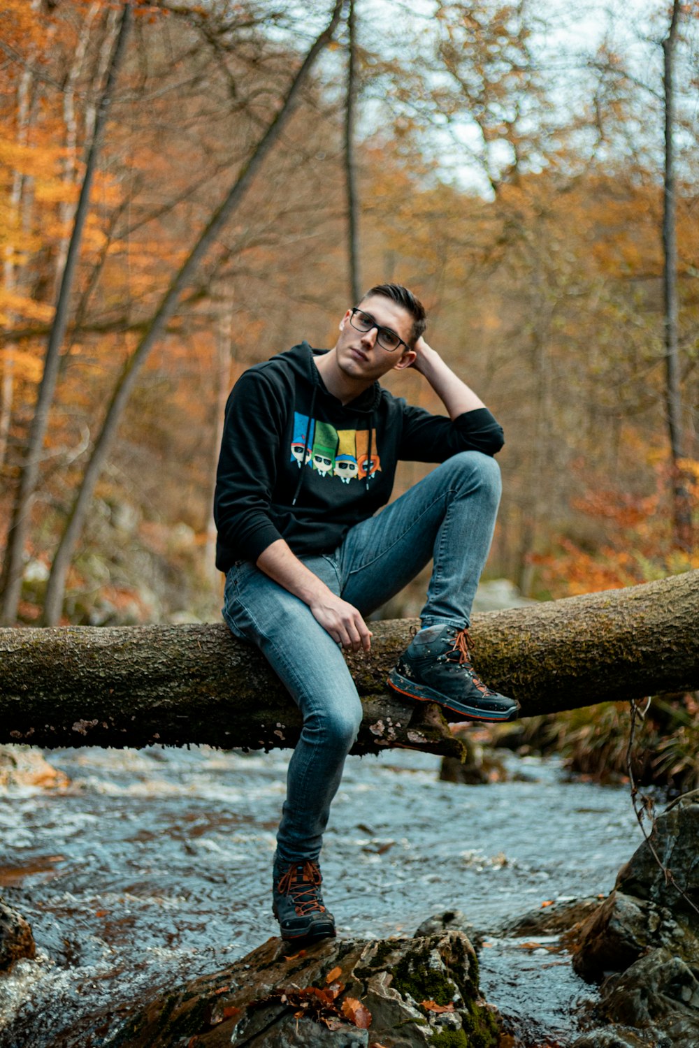 man in black crew neck t-shirt and blue denim jeans sitting on brown tree trunk