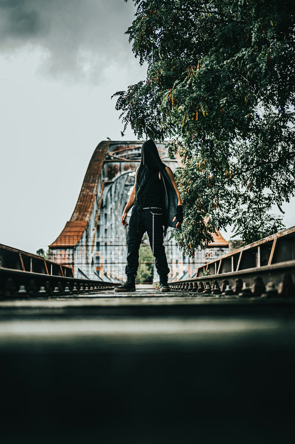 Mann in schwarzer Jacke und schwarzer Hose, der tagsüber auf der Brücke steht