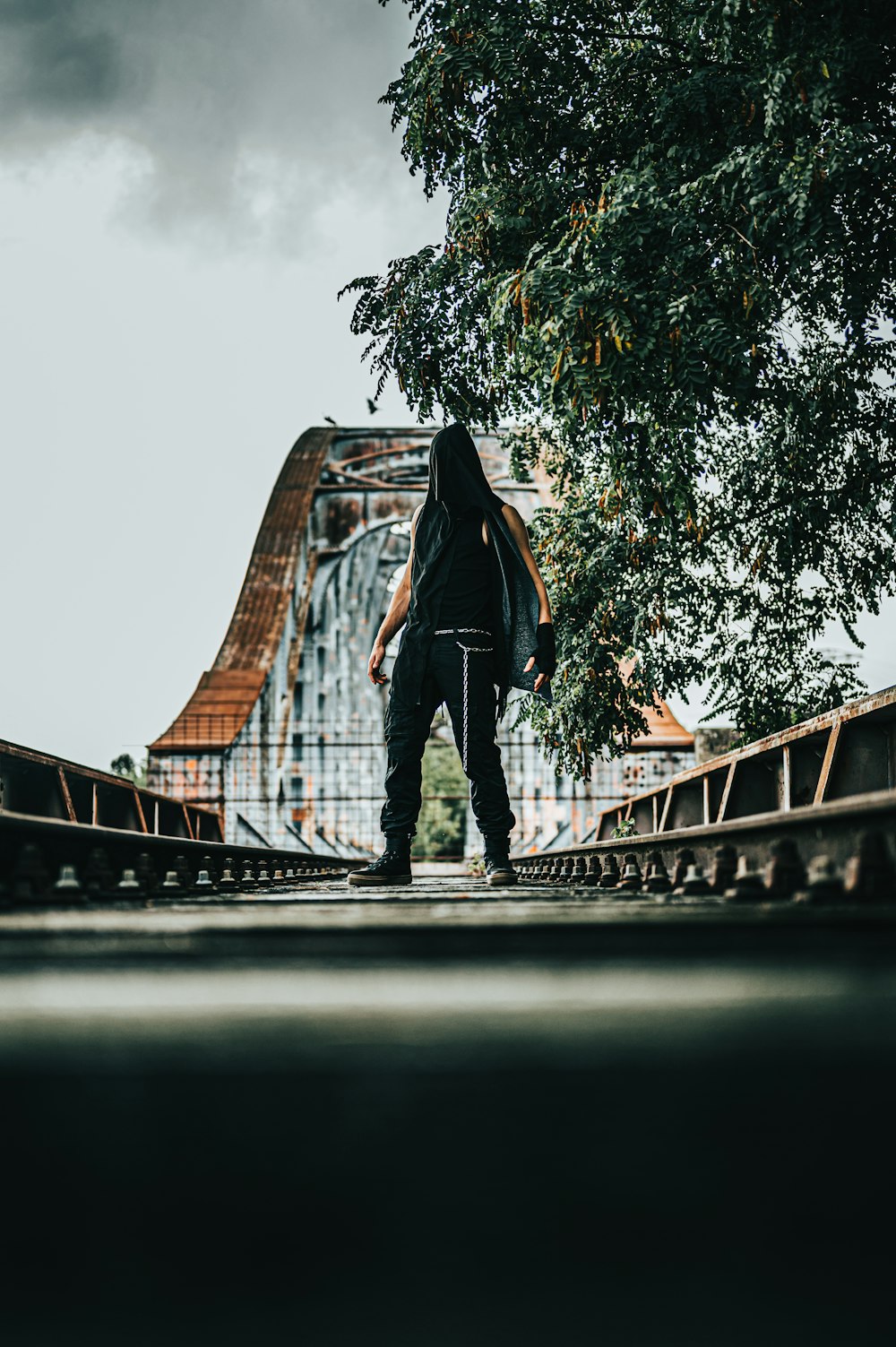 man in black jacket and black pants standing on bridge during daytime