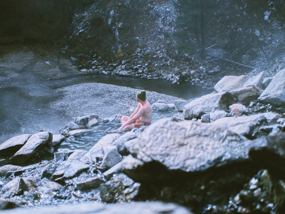 man sitting on rock in river