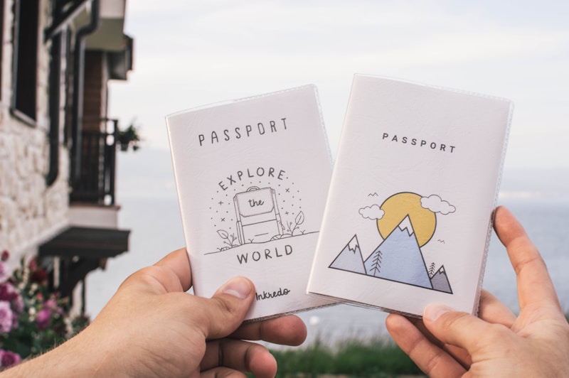 Two hands are holding up passport covers against the backdrop of a scenic lake. The left cover has an illustration of a suitcase with the words 'EXPLORE the WORLD'. The right cover features a mountain and sun illustration. There is a stone building with a rustic look on the left and flowering plants in the bottom left.