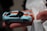 A small toy car with a Gulf oil company logo held in a person's hand. The car features a light blue body with an orange stripe running across its length. It is being held gently, with part of a white tissue or cloth visible underneath the hand.