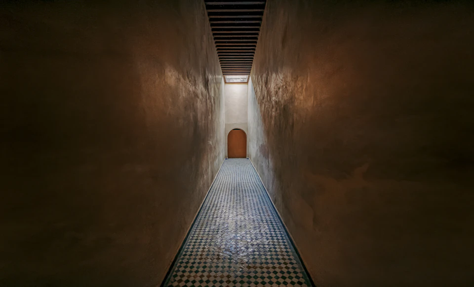 Long, narrow hallway with warm brown walls and tiled floor illuminated by natural light