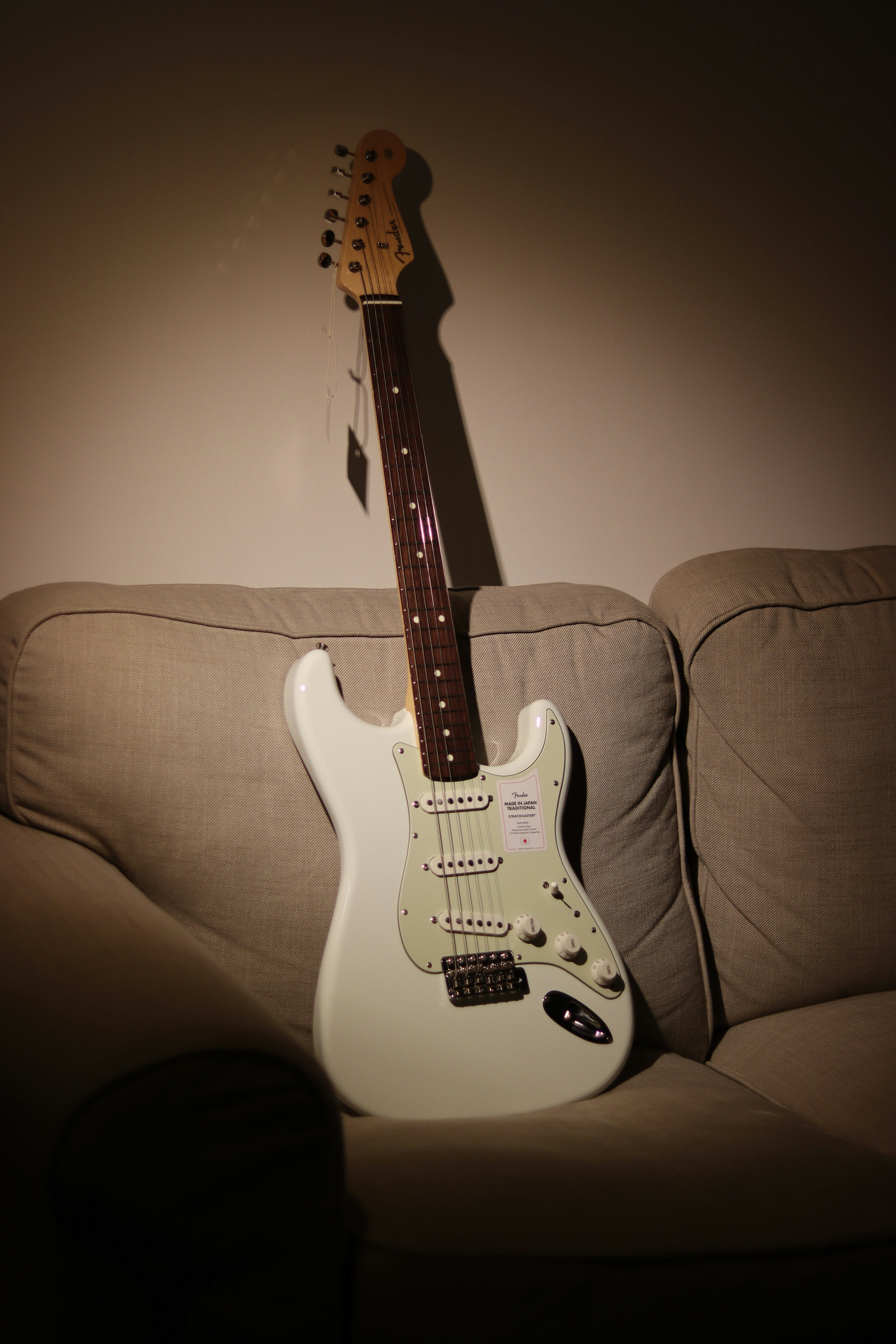 Gitar listrik Stratocaster putih dan coklat di sofa coklat