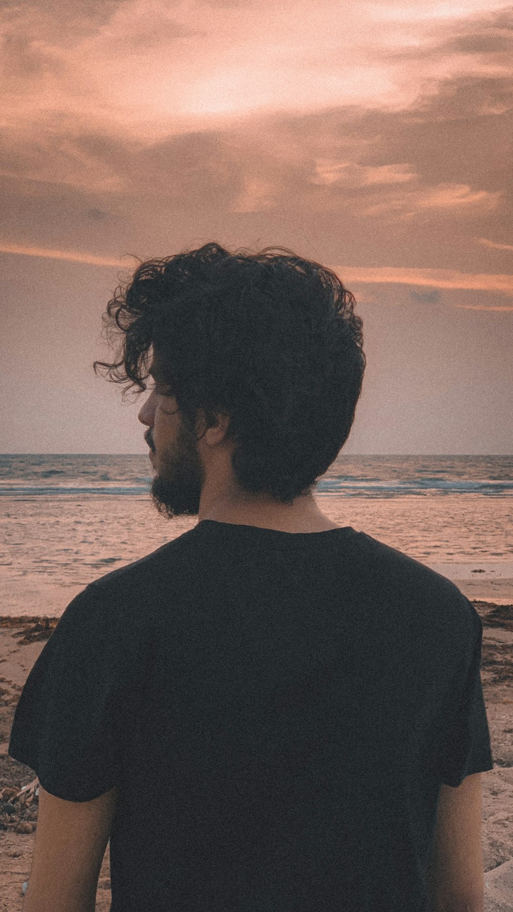 man in black shirt standing on beach during sunset