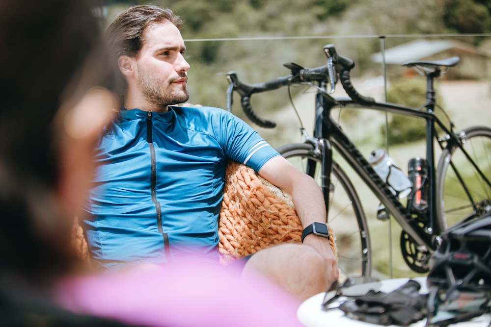 man in blue dress shirt sitting beside black bicycle