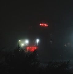 A dimly lit motel sign flickering against a foggy night sky.