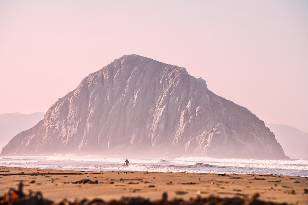 person surfing on sea near gray rock formation during daytime