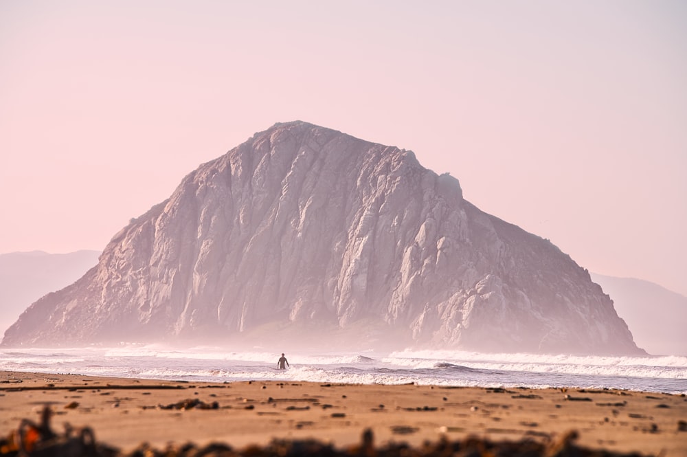 Persona che fa surf sul mare vicino alla formazione rocciosa grigia durante il giorno