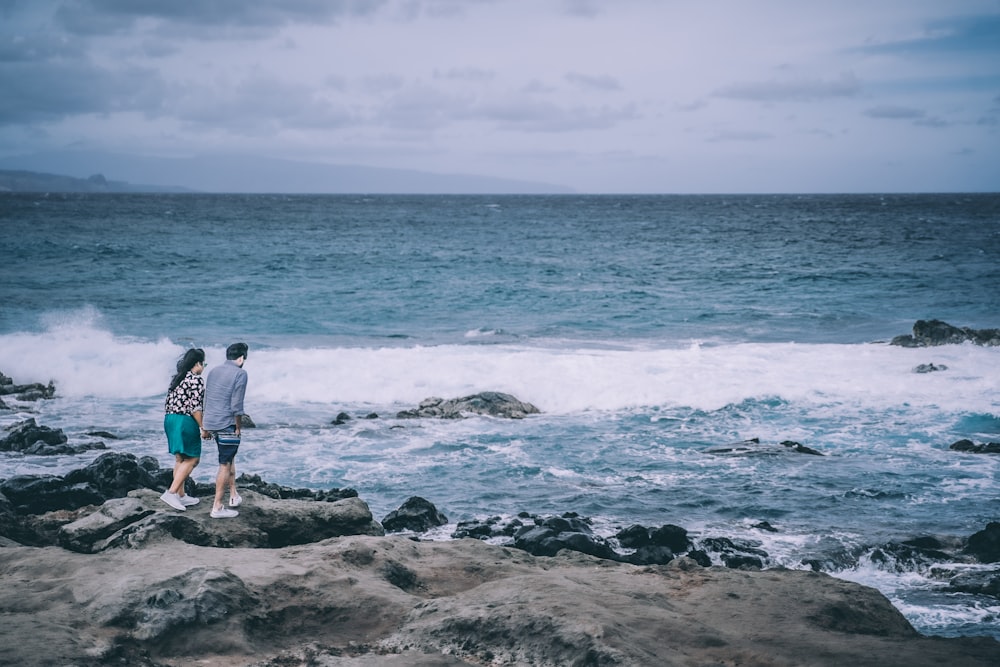 2 person standing on rocky shore during daytime