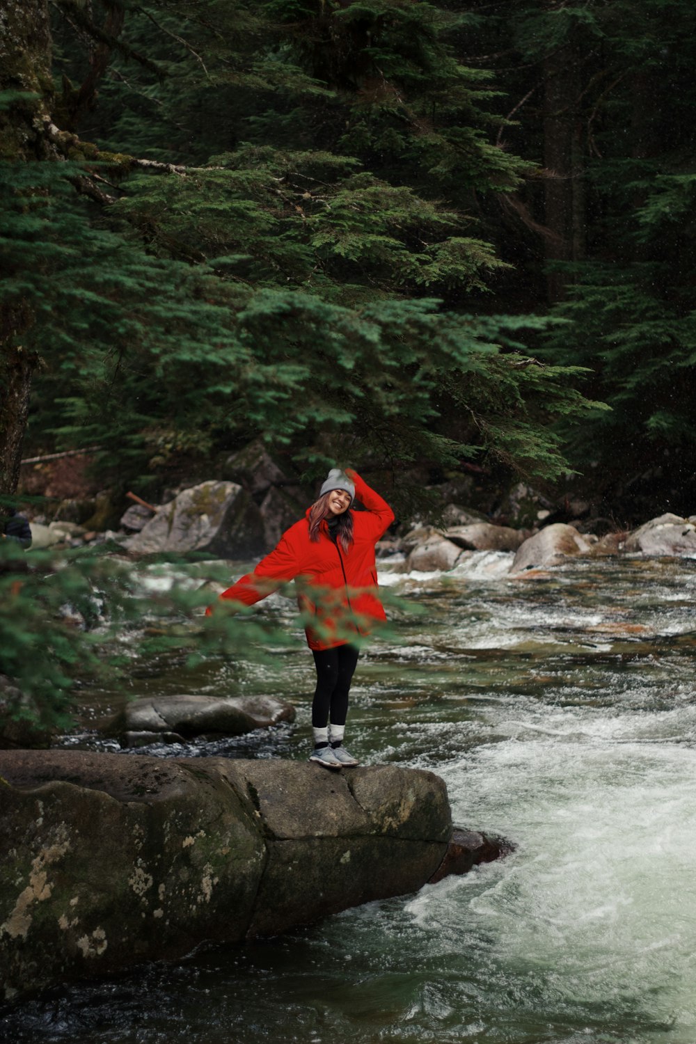 a woman in a red jacket standing on a rock in a river