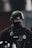 A police officer wearing tactical gear, including a black helmet and a face cover, is seen. The officer's uniform displays a police badge and has various equipment attached, including a radio and other tactical gear.