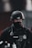 A police officer wearing tactical gear, including a black helmet and a face cover, is seen. The officer's uniform displays a police badge and has various equipment attached, including a radio and other tactical gear.