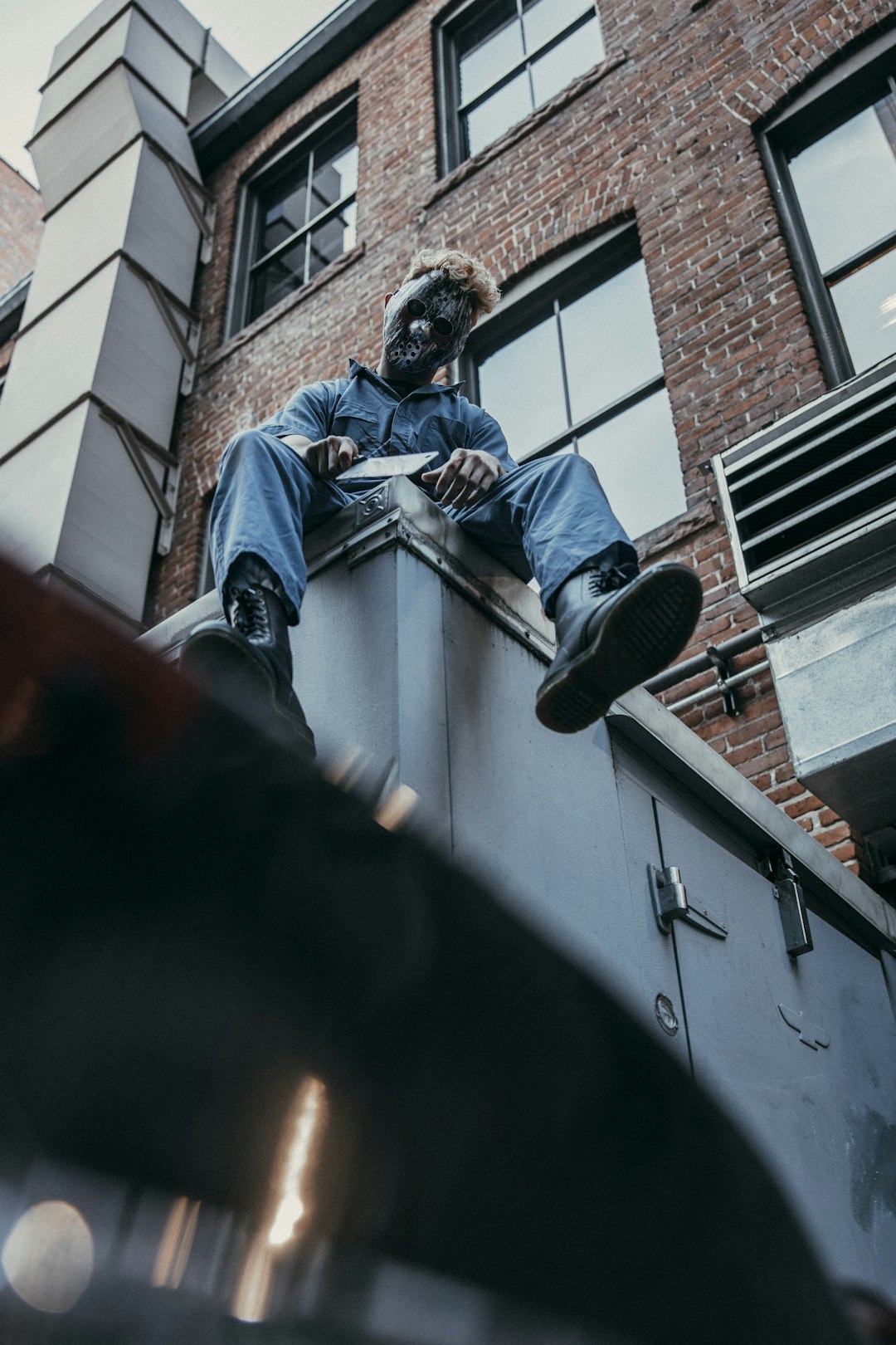 man in blue denim jacket and black cap sitting on concrete wall during daytime