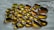 A collection of polished, translucent stones or beads with a glossy surface, arranged on a textured white surface. The stones display a rich, golden-amber hue with subtle gradients, creating a smooth and reflective appearance.