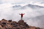 person in red long sleeve shirt standing on brown rock formation during daytime
