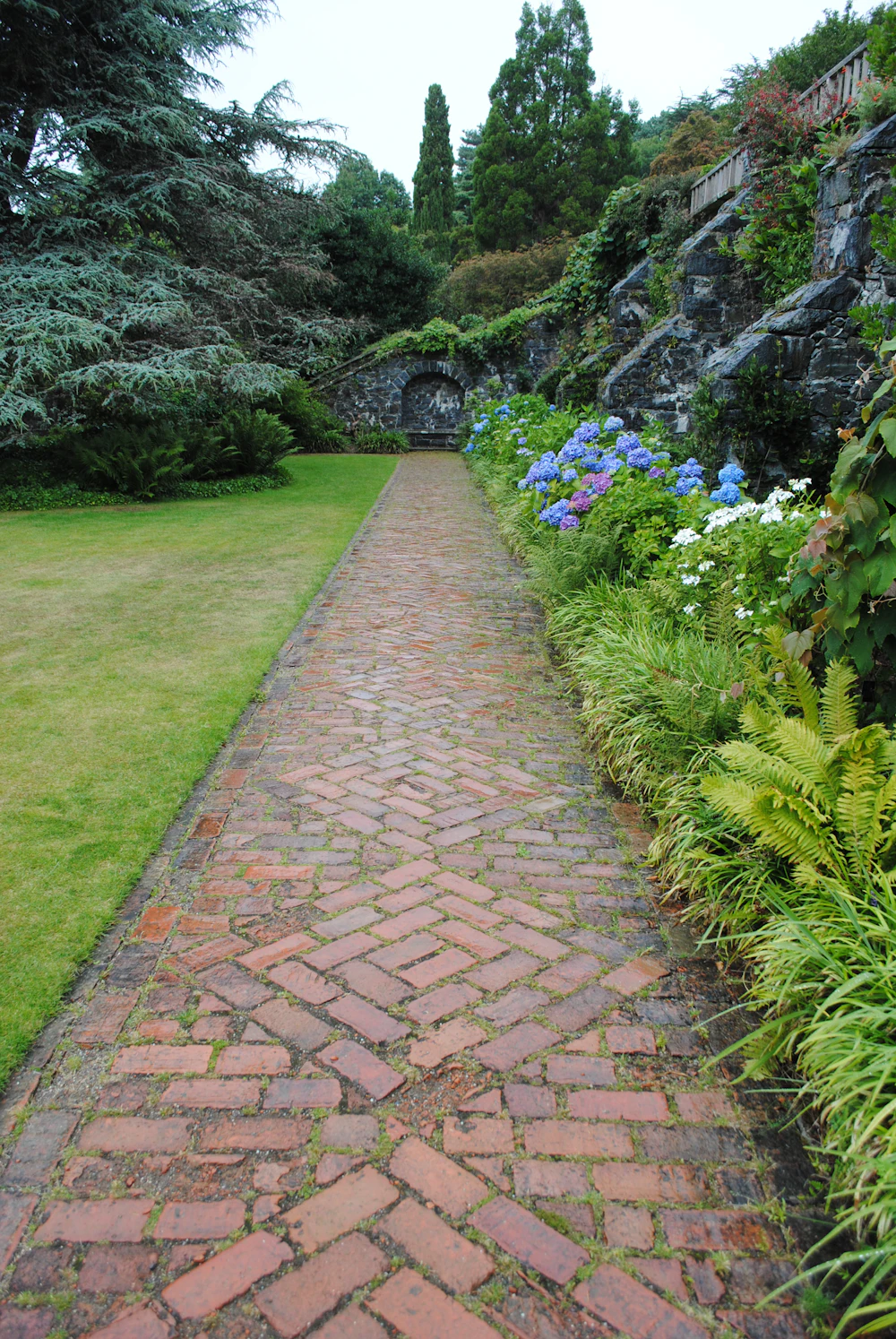 A herringbone clay paver path running between a lawn and a planted border