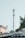 A telecommunications tower rises prominently against a pale sky. It is surrounded by lush green foliage and the edge of a building is visible on the left side. The scene also includes parts of a rooftop at the bottom.