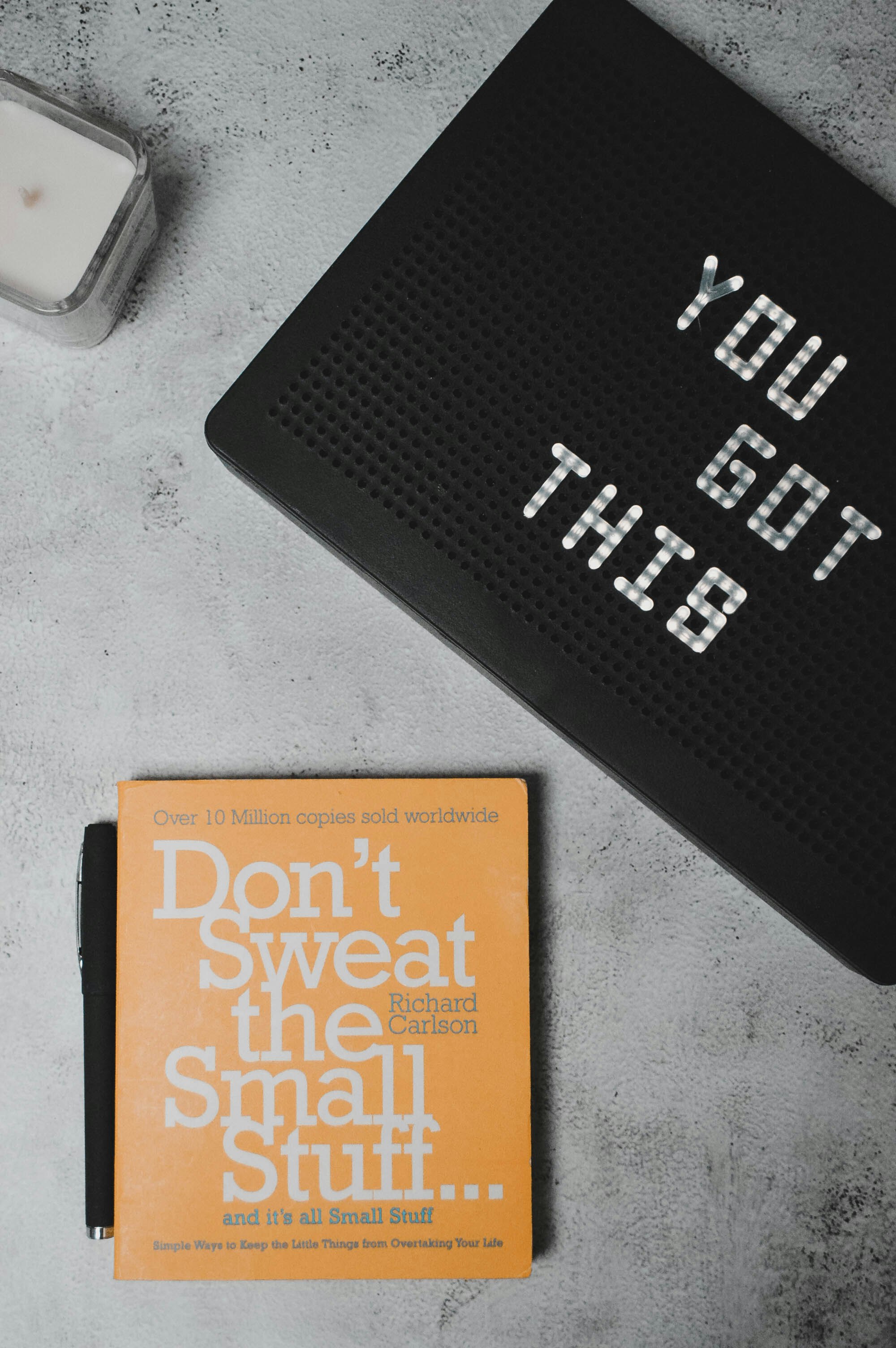 Flatlay of a book "Don't sweat the small stuff ... and it's all small stuff" beside a motivational sign